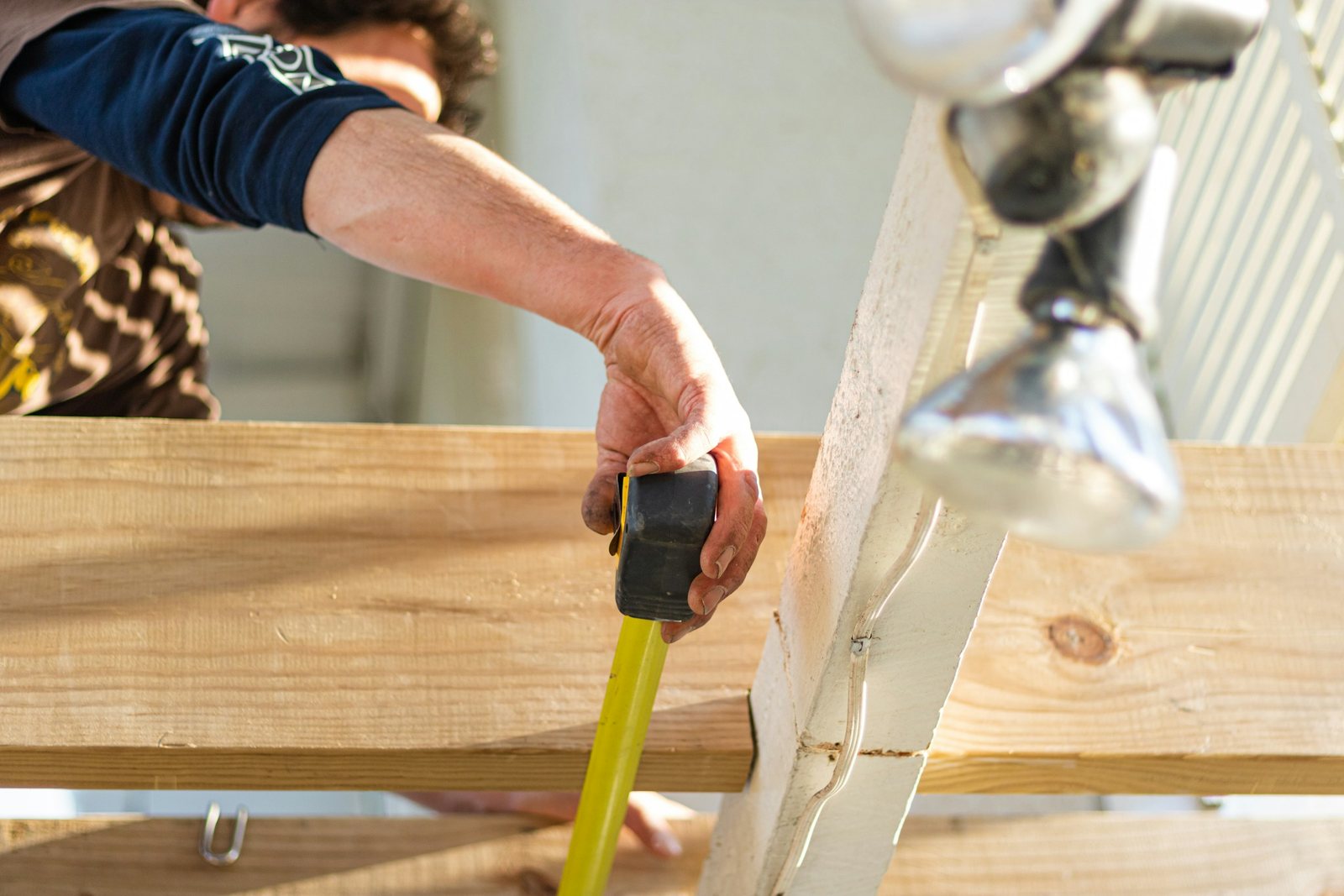 Carpenter measuring timber deck framing with a tape measure during a renovation