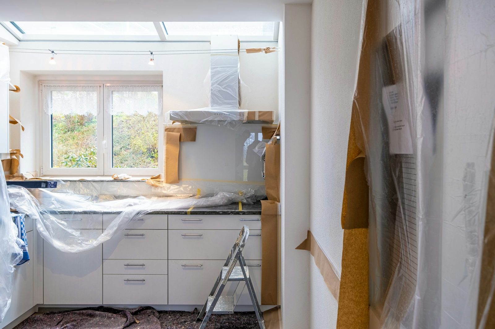 Kitchen mid-renovation with new white cabinetry protected by plastic sheeting