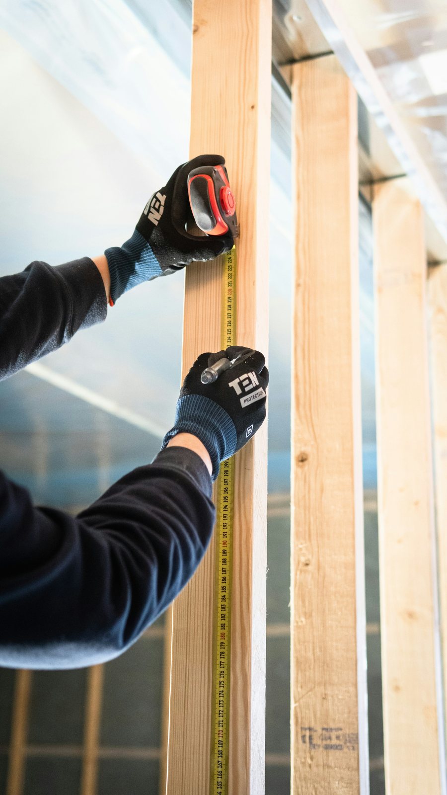 Carpenter measuring a timber wall stud with a tape measure during structural framing